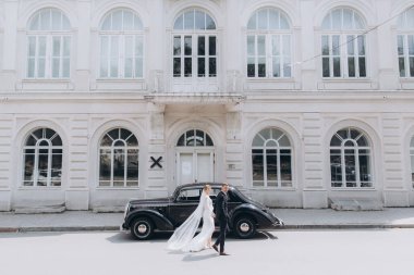 Güzel, şık bir çiftin düğünü, beyaz gelinlikli bir gelin ve siyah takım elbiseli bir damat, smokin, siyah bir retro araba..