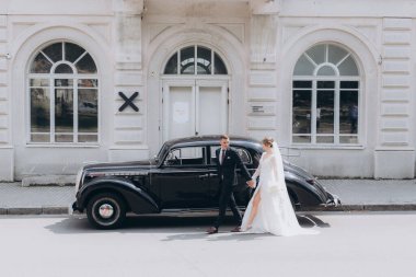 Güzel, şık bir çiftin düğünü, beyaz gelinlikli bir gelin ve siyah takım elbiseli bir damat, smokin, siyah bir retro araba..