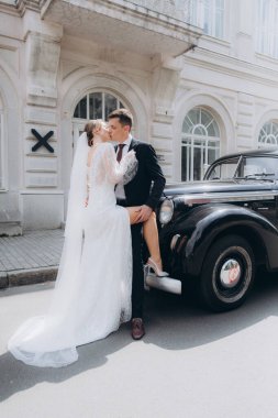 Güzel, şık bir çiftin düğünü, beyaz gelinlikli bir gelin ve siyah takım elbiseli bir damat, smokin, siyah bir retro araba..