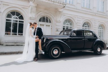 Güzel, şık bir çiftin düğünü, beyaz gelinlikli bir gelin ve siyah takım elbiseli bir damat, smokin, siyah bir retro araba..