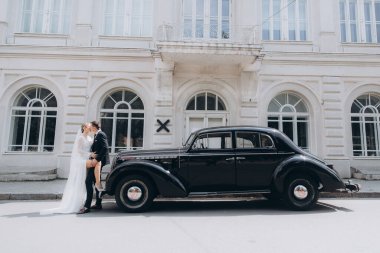 Güzel, şık bir çiftin düğünü, beyaz gelinlikli bir gelin ve siyah takım elbiseli bir damat, smokin, siyah bir retro araba..