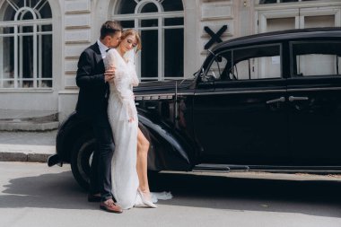 Güzel, şık bir çiftin düğünü, beyaz gelinlikli bir gelin ve siyah takım elbiseli bir damat, smokin, siyah bir retro araba..