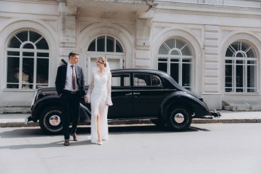 Güzel, şık bir çiftin düğünü, beyaz gelinlikli bir gelin ve siyah takım elbiseli bir damat, smokin, siyah bir retro araba..