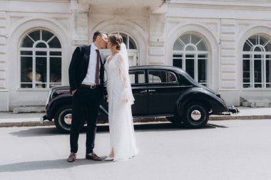 Güzel, şık bir çiftin düğünü, beyaz gelinlikli bir gelin ve siyah takım elbiseli bir damat, smokin, siyah bir retro araba..