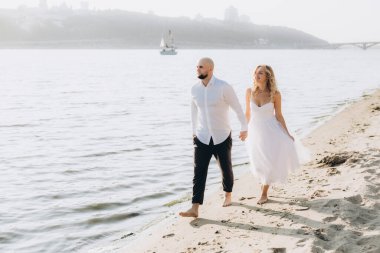 Wedding photosession at sunset of a beautiful couple, the bride in a white dress, and the groom in a white shirt and black trousers