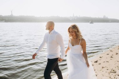 Wedding photosession at sunset of a beautiful couple, the bride in a white dress, and the groom in a white shirt and black trousers