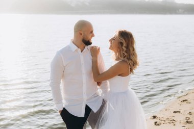 Wedding photosession at sunset of a beautiful couple, the bride in a white dress, and the groom in a white shirt and black trousers