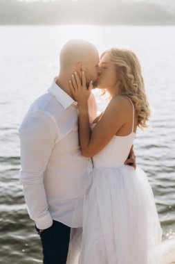 Wedding photosession at sunset of a beautiful couple, the bride in a white dress, and the groom in a white shirt and black trousers