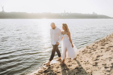 Wedding photosession at sunset of a beautiful couple, the bride in a white dress, and the groom in a white shirt and black trousers