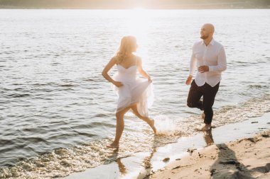 Güzel bir çiftin gün batımında düğün fotoğrafları, beyaz elbiseli gelin, beyaz gömlekli ve siyah pantolonlu damat.