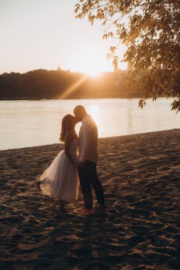 Güzel bir çiftin gün batımında düğün fotoğrafları, beyaz elbiseli gelin, beyaz gömlekli ve siyah pantolonlu damat.