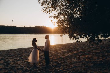 Güzel bir çiftin gün batımında düğün fotoğrafları, beyaz elbiseli gelin, beyaz gömlekli ve siyah pantolonlu damat.