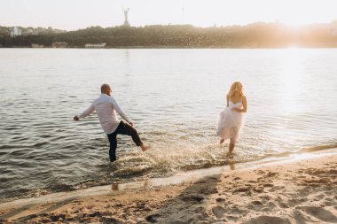 Güzel bir çiftin gün batımında düğün fotoğrafları, beyaz elbiseli gelin, beyaz gömlekli ve siyah pantolonlu damat.