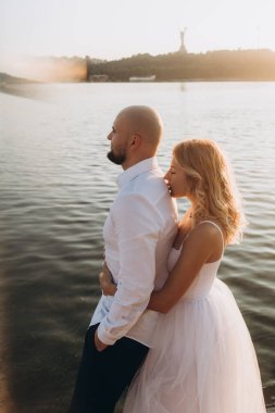 Güzel bir çiftin gün batımında düğün fotoğrafları, beyaz elbiseli gelin, beyaz gömlekli ve siyah pantolonlu damat.