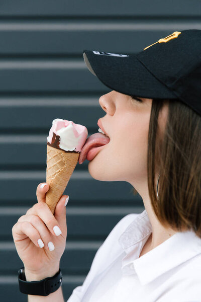 Brunette girl in a cap and shirt eats fun ice cream