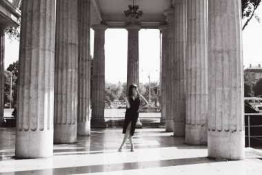 Siyah elbiseli, güzel bir kız elinde sigarasıyla sokakta sigara içiyor, siyah beyaz bir fotoğraf..