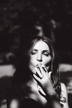Siyah elbiseli, güzel bir kız elinde sigarasıyla sokakta sigara içiyor, siyah beyaz bir fotoğraf..