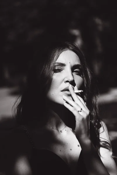 一个漂亮的姑娘 穿着黑色的衣服 手里拿着香烟 在街上抽烟 脸上挂着黑白照片 — 图库照片