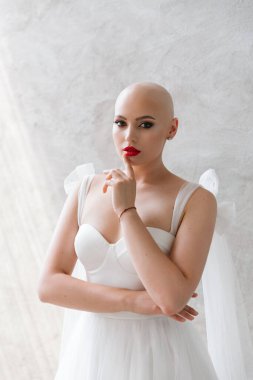 Bald beautiful bride in a luxurious wedding dress in red lipstick and a long veil is sick with cancer