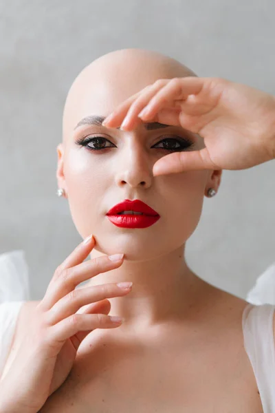 Bald beautiful bride in a luxurious wedding dress in red lipstick and a long veil is sick with cancer