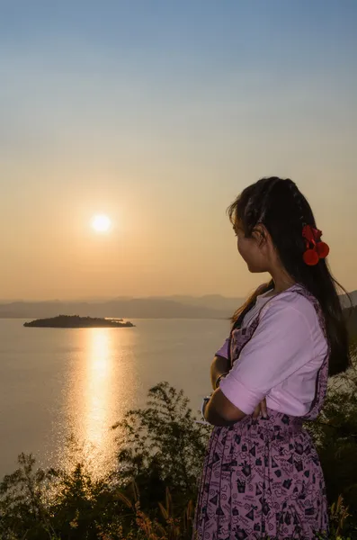 Счастливая молодая женщина стоит и смотрит на закат над озером — стоковое фото