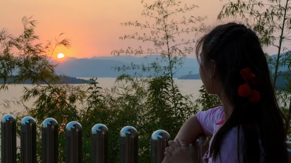 Счастливая молодая женщина стоит и смотрит на закат над озером — стоковое фото