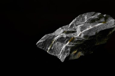 Makro, siyah yansıtıcı arka planda izole edilmiş hammadde Manganez Ore kayasının görüntüsünü kapat