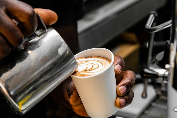 African Coffee Barista pouring a heart shape design with milk foam