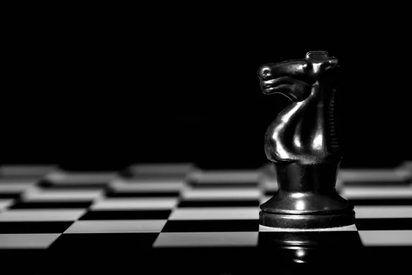 Close up of Chess pieces on a reflective mirror board surface with a plain black background