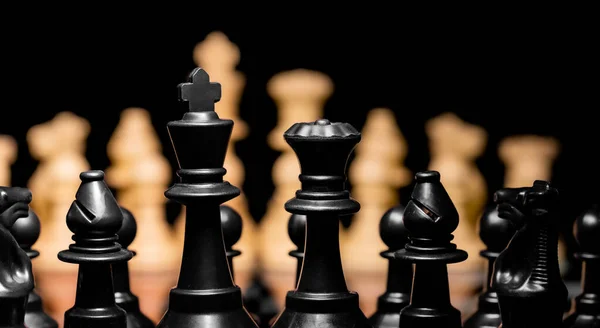 Close up of Chess pieces on a reflective mirror board surface with a plain black background