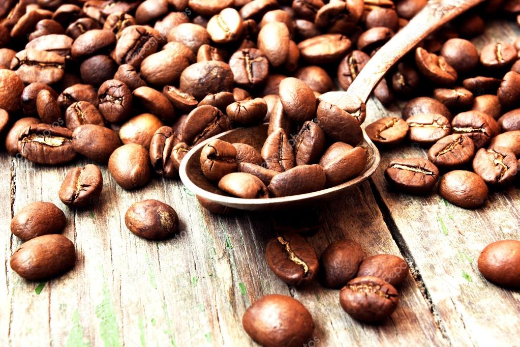 Roasted coffee beans in a spoon on wooden background