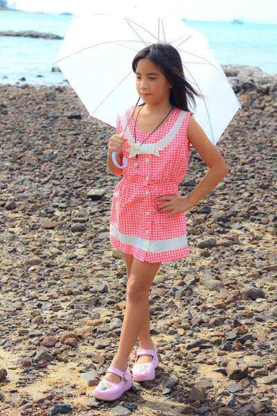 Kleine asiatische Mädchen mit rosa Kleid steht auf dem Felsen am Strand — Stockfoto