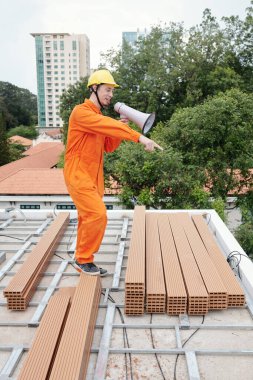 Foreman hoparlörle çatıda dikiliyor.