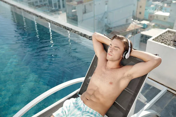 Joven escuchando música en la piscina — Foto de Stock