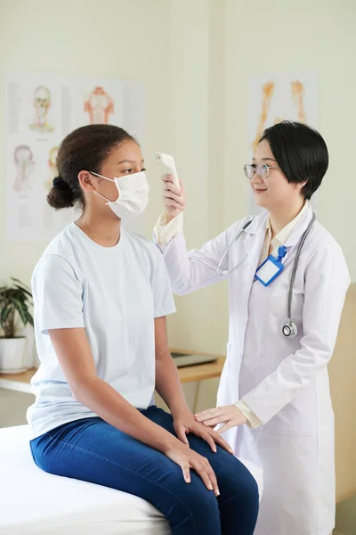 Lekarz sprawdzający temperaturę ciała nastolatki — Zdjęcie stockowe