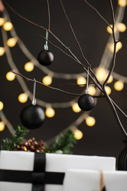 Ağaç dallarında asılı siyah mat ve ışıltılı mücevherler ve arka planda Noel ışıkları
