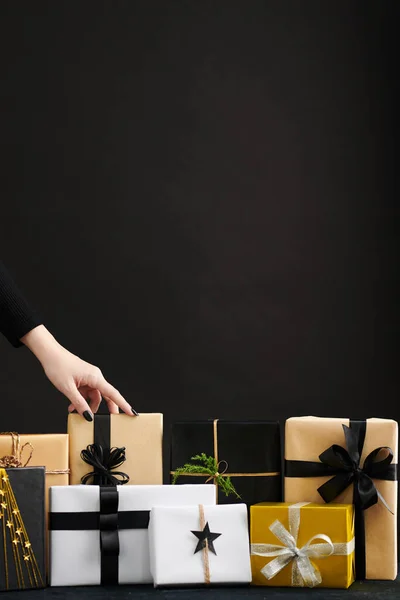 女人的手把礼物包在一堆黑色 米黄色和金色的圣诞礼物里 — 图库照片