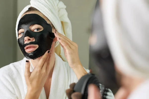 Femme appliquant masque feuille noire — Photo
