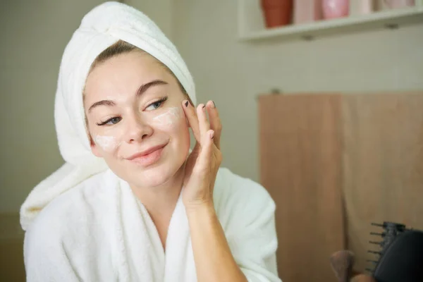 Giovane donna che applica la crema viso — Foto Stock