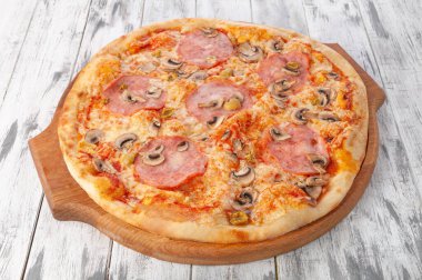 Jambonlu ve mantarlı pizza, domates sosu ve mozzarella peyniri. Yuvarlak tahta. Hafif ahşap zemin. Yukarıdan görüntüle.