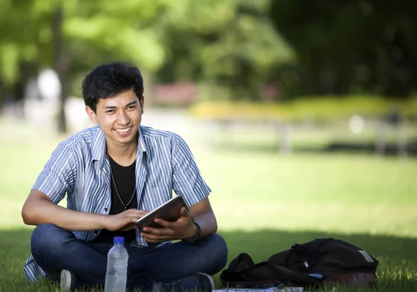 Asiatisk manlig student använder tablet i soliga gräsmark område — Stockfoto