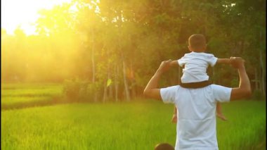 Üç yaşında bir çocuk ailesinin omuzlarında oturuyor. Mutlu aile kavramı