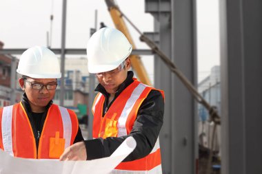 two construction workers or foreman discussing on location site with crane in the background