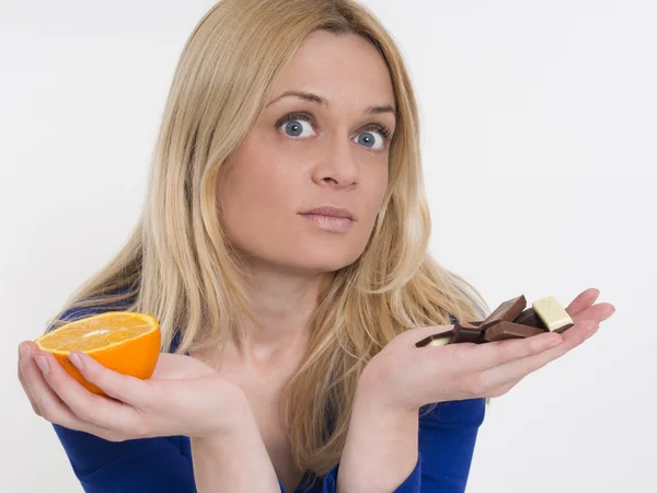 Mujer con naranjas sanas en una mano y chocolate en otra —  Fotos de Stock