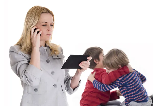 Ocupada madre con tableta y móvil mientras sus hijos pelean — Foto de Stock