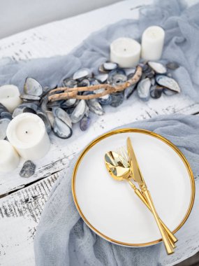 Deniz usulü konforlu masa, mumlar, midye kabukları ve gri-mavi renkli peçeteler. Nişan, düğün, romantik yemek ya da şenlik için servis edilen masa. Açık hava ya da yemek servisi..