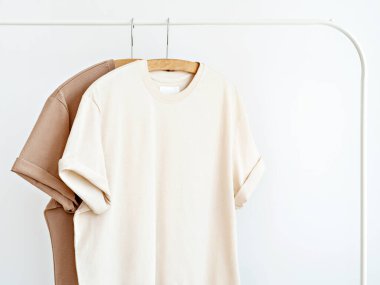 Tarafsız sütlü iki tişört beyaz duvara karşı beyaz askıda asılı. Boş şablon, tekstil tasarımı için model. Yaz minimalist kıyafet fikri. Kapsül dolabı.