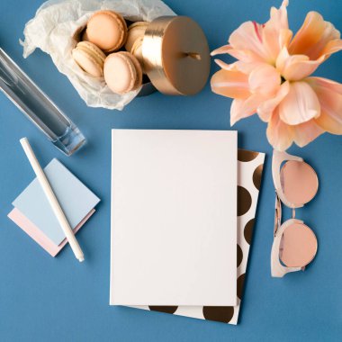 Yukardan gelen serbest çalışan kızlar için ev ofis çalışma alanı. Defterleri, kalemleri, klasik güneş gözlükleri, pembe çiçekleri ve mavi arka planda kurabiyeleri olan kırtasiye malzemesi dairesi. Boş mandıra, çizim, notlar şablon.