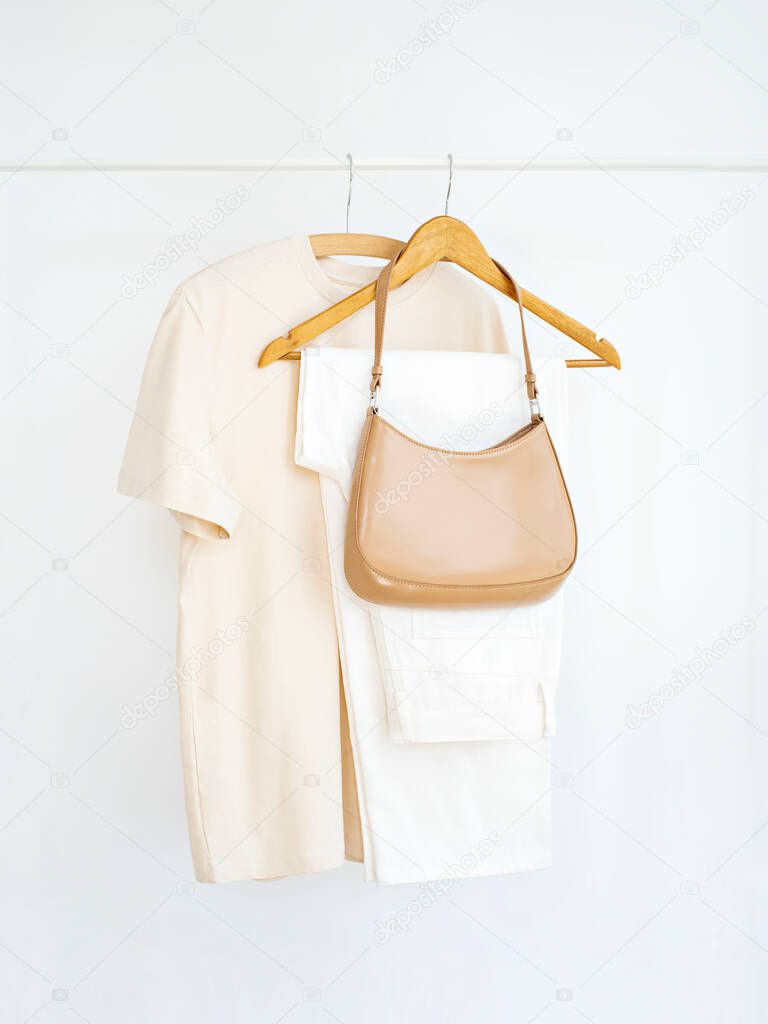 Woman's cotton casual outfit in shades of beige on white background. Rack with summer female clothes on hangers next to wall. Clothing retails concept. Advertise, sale, fashion. Simplicity concept.