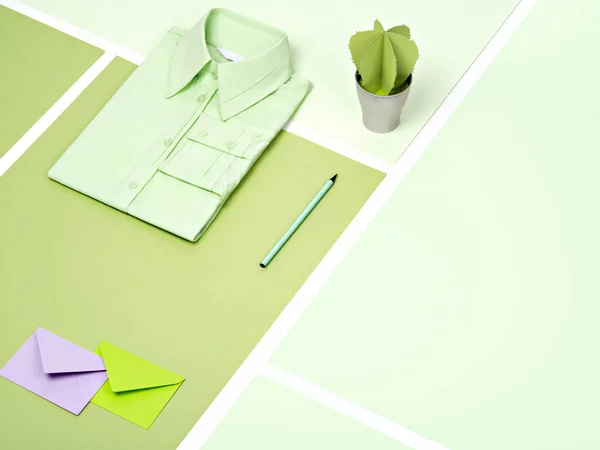 Mint green plain cotton formal shirt, stationary and artificial succulent arranged on a various green paper background. Trendy office outfit or minimalist clothing concept with copy space.